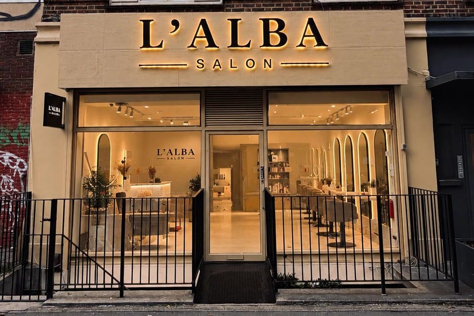 The L'ALBA salon on Eversholt Street at dusk: the glowing gold sign above windows with arched mirrors